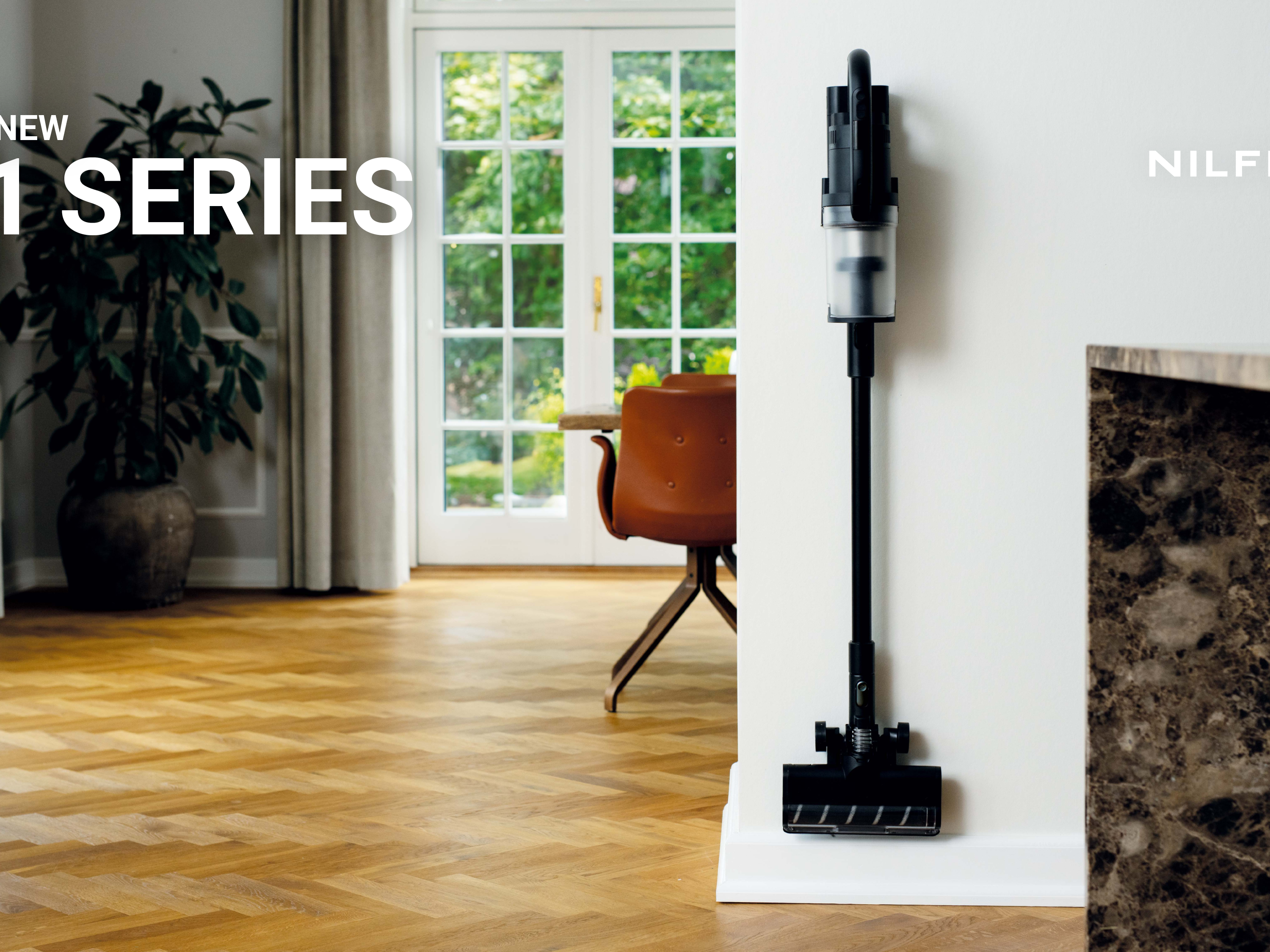 Sleek black cordless vacuum mounted on white wall in bright, modern living room with wooden floors and greenery.