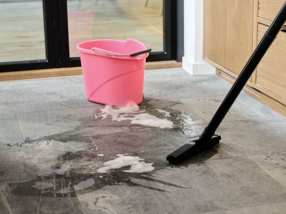 Black wet/dry vacuum cleaning soapy water spill on gray tile floor near pink bucket.