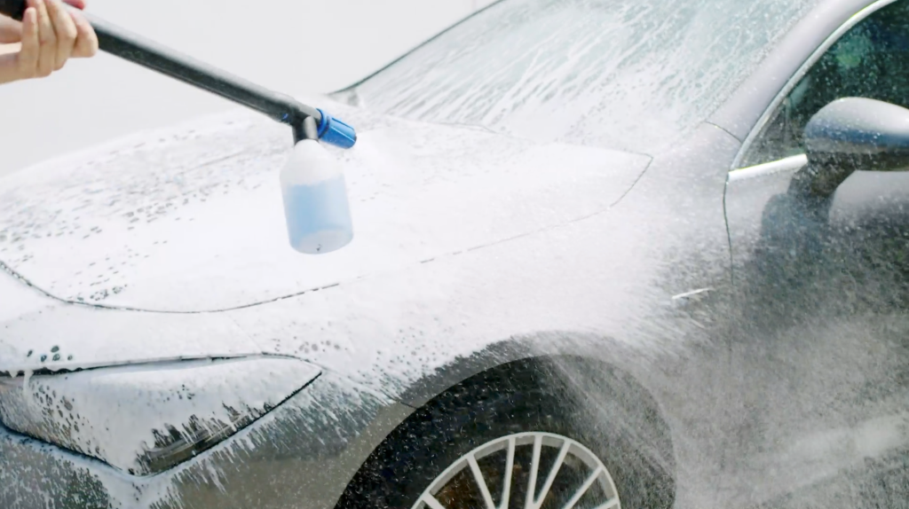 High-pressure cleaner detergent, 500 ml, with white foam being sprayed on a gray car.