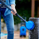 Rotating brush accessory for pressure washers, alongside denim-clad person cleaning furniture.