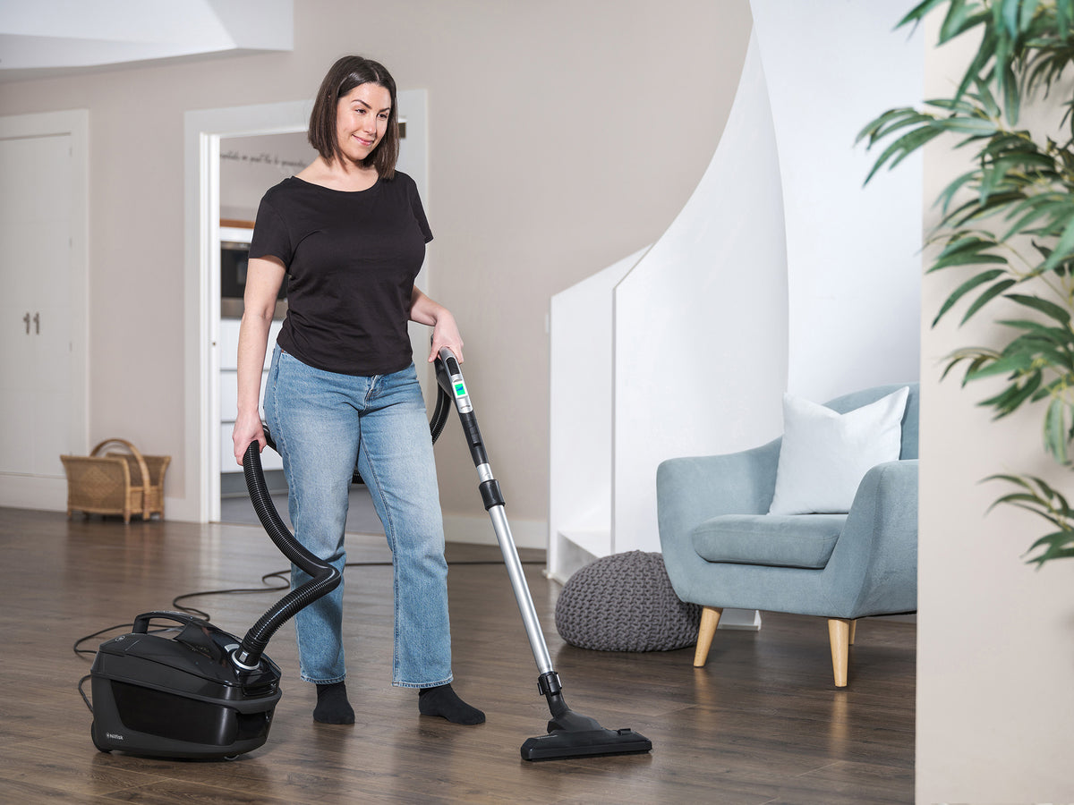 Vacuum cleaner with a black casing by Nilfisk, being used inside a modern home.