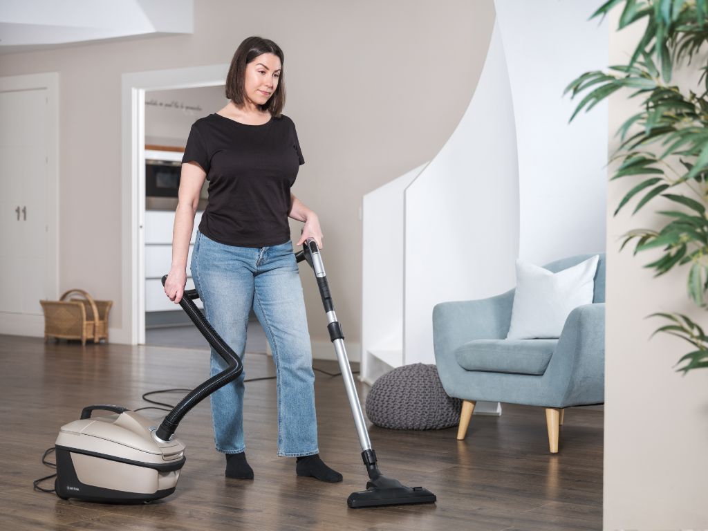 Champagne-colored canister vacuum cleaner by Nilfisk, with a black hose and silver wand on a wood floor.