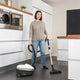 Bagless vacuum cleaner by Nilfisk being used in a modern white kitchen, with dark gray floors and a woman vacuuming.