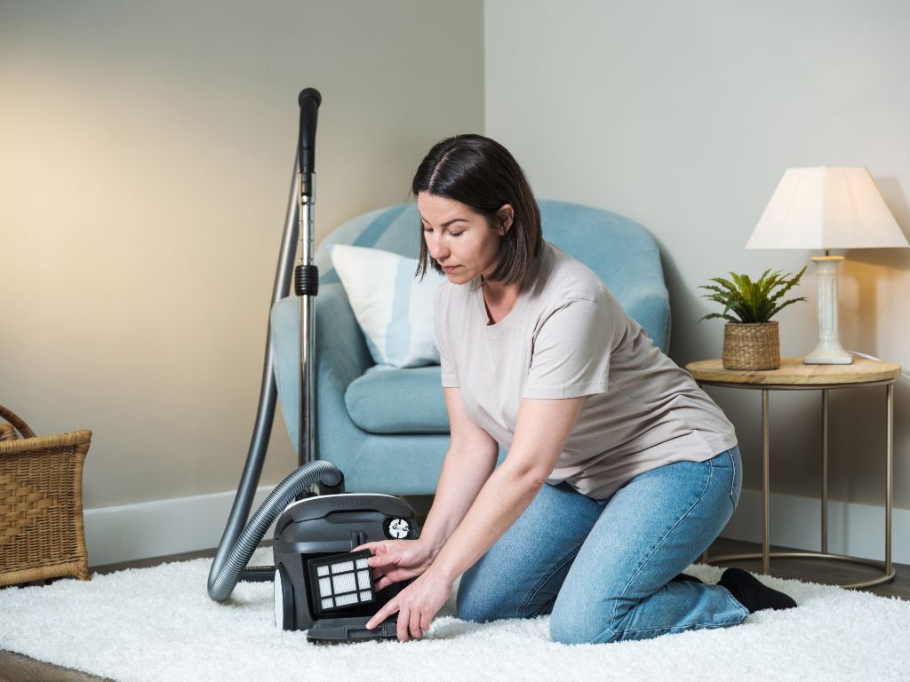 Black canister vacuum cleaner by ES One Pet Care 750 W, shown in lifestyle use on white rug with filter access, side view