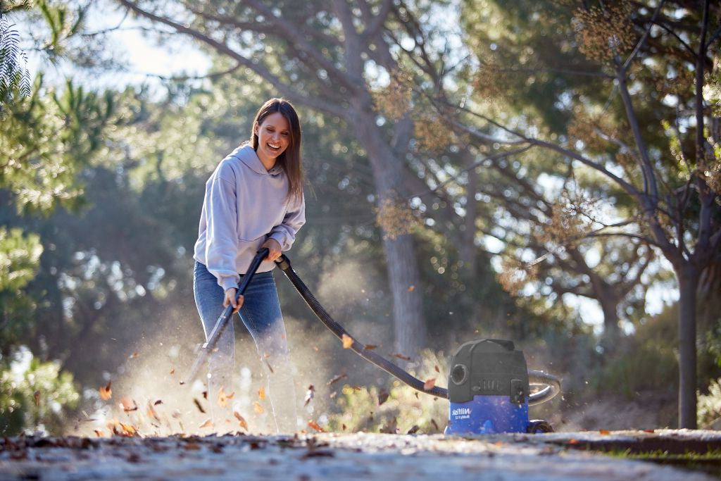 Wet and dry vacuum cleaner by Nilfisk being used to vacuum leaves outdoors, worn with a light purple hoodie and jeans.