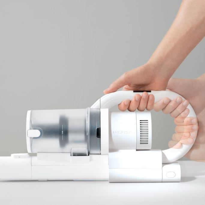 White cordless stick vacuum cleaner by Nilfisk, being held by a hand, showcasing its compact design.