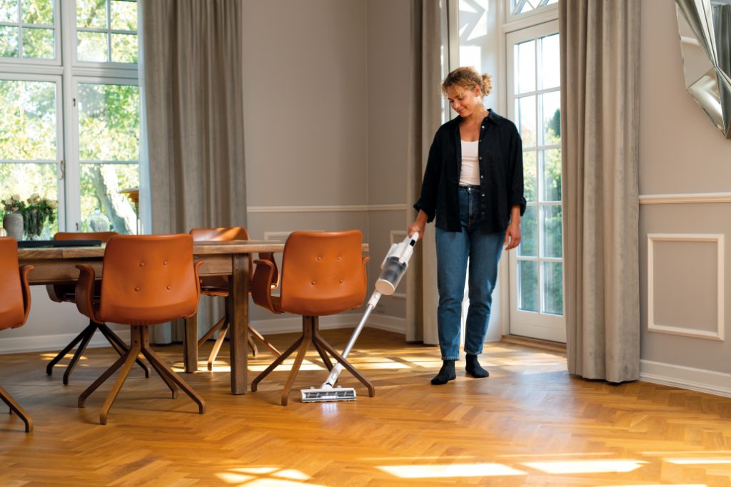 Cordless stick vacuum by HOME ES in use on a wood herringbone floor.