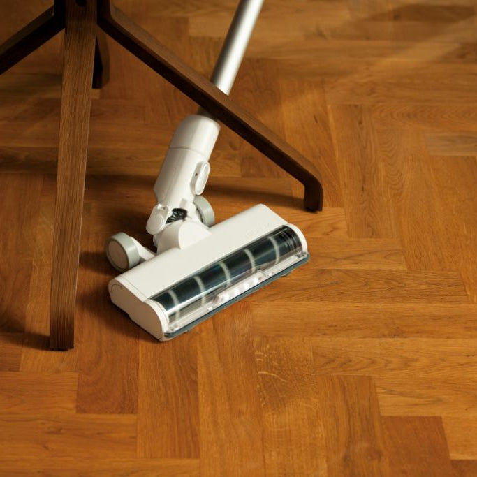 Cordless stick vacuum with a brush head attachment by HOME, on a wooden herringbone floor.
