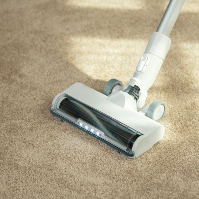 White cordless stick vacuum cleaner by Nilfisk with LED lights on a beige carpet.