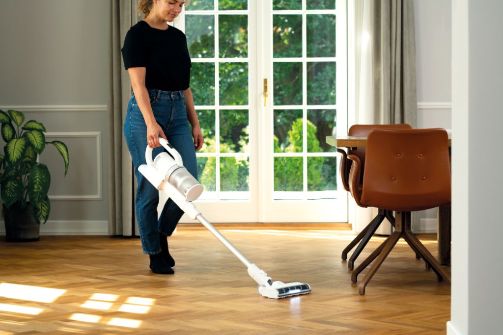 Cordless stick vacuum cleaner by Allergy, with LED lighting, held on a herringbone hardwood floor.