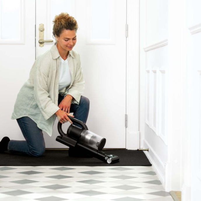 Cordless stick vacuum cleaner 550 W with LED from PET CARE, held by a woman in a bright hallway.