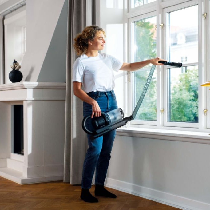 Cordless stick vacuum cleaner with LED lighting by [Vendor name], held by a woman in a living room.