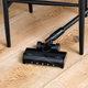 Black cordless vacuum cleaner with docking station, 150 W, on wooden floor, side view, LED lights on brush head
