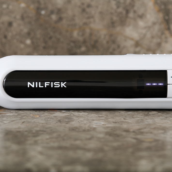 White handheld vacuum cleaner by Nilfisk with black grip panel, power buttons, and blue LED display, side view on stone surface