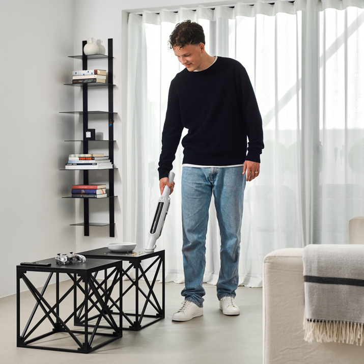 White handheld vacuum cleaner by Spot in use on coffee table, lifestyle view, modern living room setting