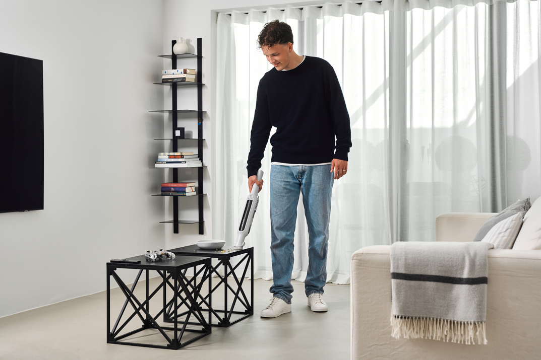 White handheld vacuum cleaner by Spot in use on coffee table, lifestyle view, modern living room setting
