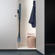 Blue cordless stick vacuum cleaner by Move stored upright in white closet, next to woven basket and hanging navy shirt, side view.