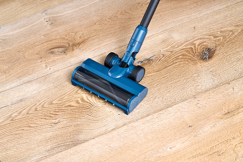 Blue cordless stick vacuum cleaner by Move with black brush roll and wheels, shown on light wooden floor from side angle