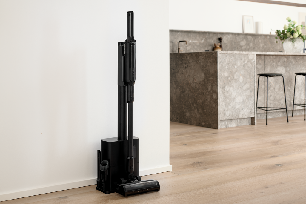 Black cordless stick vacuum with docking station by Move, upright on wooden floor in modern kitchen, side view