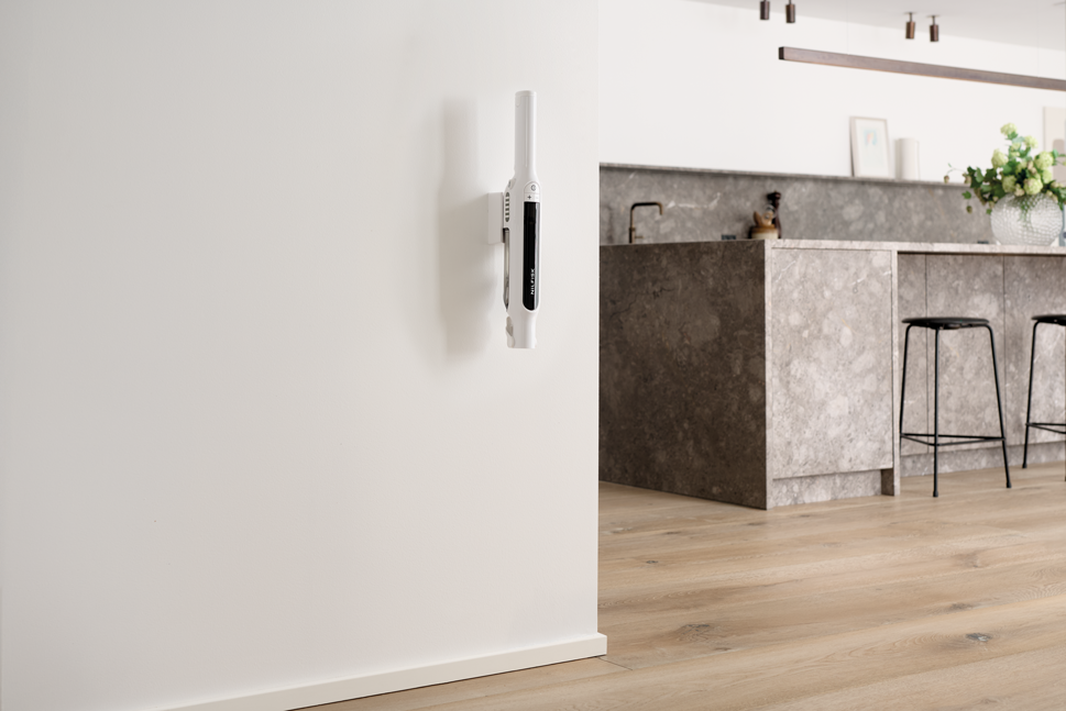 White handheld vacuum cleaner by Spot mounted on wall in modern kitchen, sleek design with black accent panel, side view
