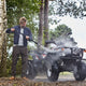 Black high-pressure washer with long hose and spray nozzle in use, cleaning ATV outdoors, side view, water mist visible