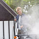 Black high-pressure washer with spray lance in use by man cleaning car, outdoor lifestyle view, water mist visible