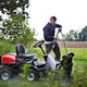 Red and black high-pressure washer by ES Premium in use, cleaning lawn mower outdoors, side view with water spray visible