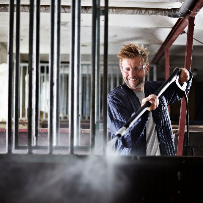 High pressure washer by Premium being used for cleaning an enclosure, featuring a man wearing safety glasses.