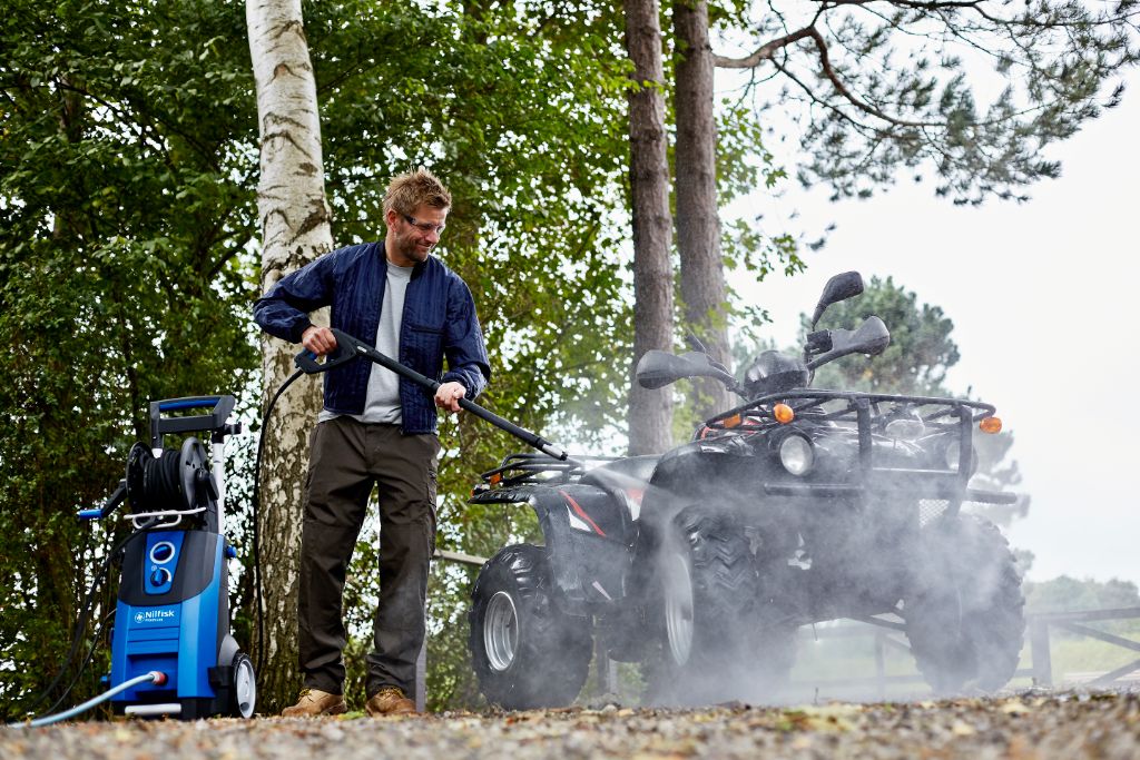High pressure washer from Nilfisk with blue housing and hose reel, in use outdoors.