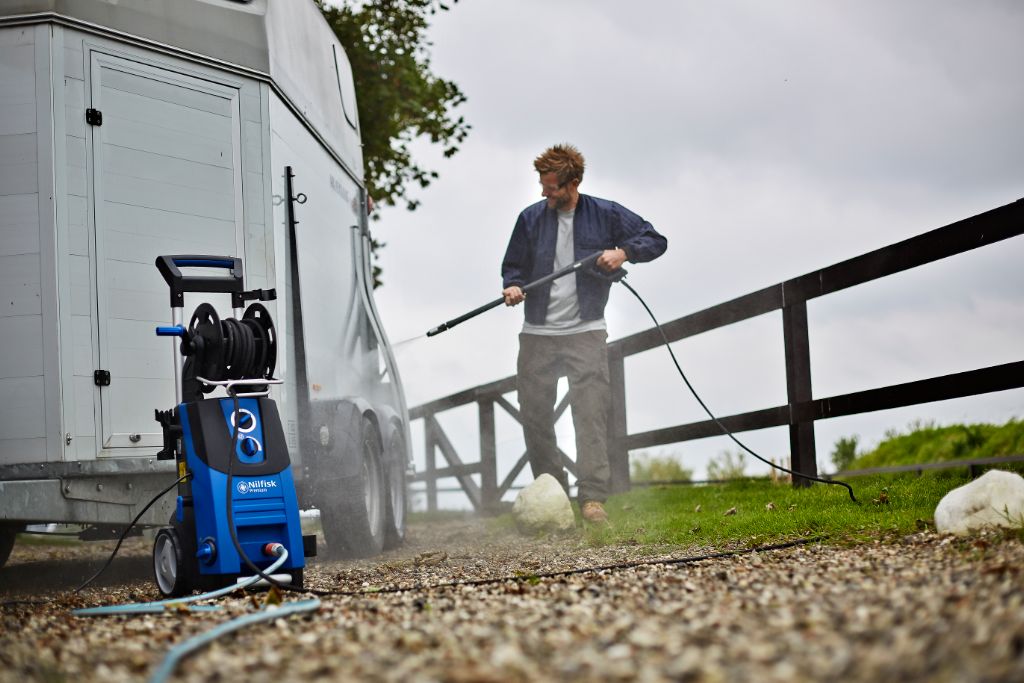 Blue high-pressure washer by Nilfisk washing a trailer with a man using the pressure nozzle.