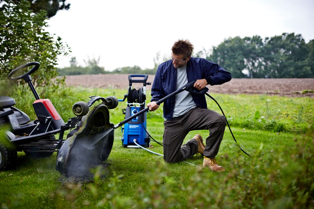 High-pressure cleaner for car washing by Nilfisk cleaning a lawnmower, shown in an outdoor lifestyle image.
