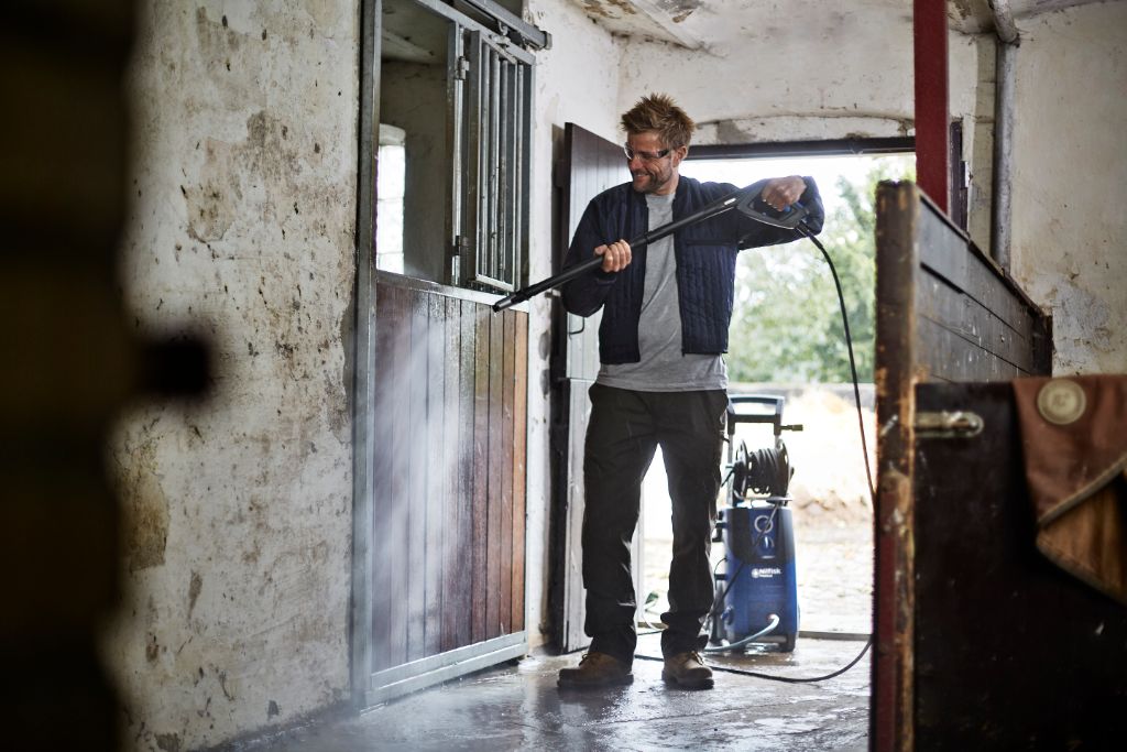 High-pressure washer, with car wash function, by Nilfisk, being used inside of a barn with a man wearing safety glasses.