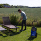 High-pressure cleaner, by Nilfisk, on a lawn next to two wooden lounge chairs, with a man using the cleaner.
