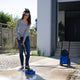 High pressure washer by Nilfisk with blue housing on a paved patio while in use by a woman.