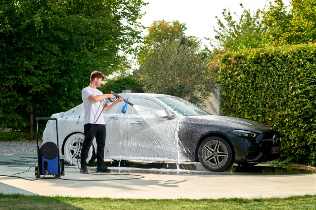 High pressure washer by Excellent 160 UK with attached hose and spray gun, washing a black car outdoors.