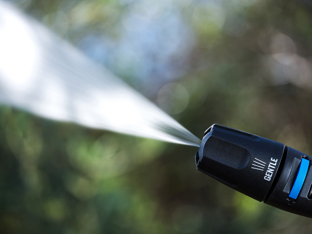 Black high-pressure washer by Nilfisk dispensing water in a garden, displayed at an angle.