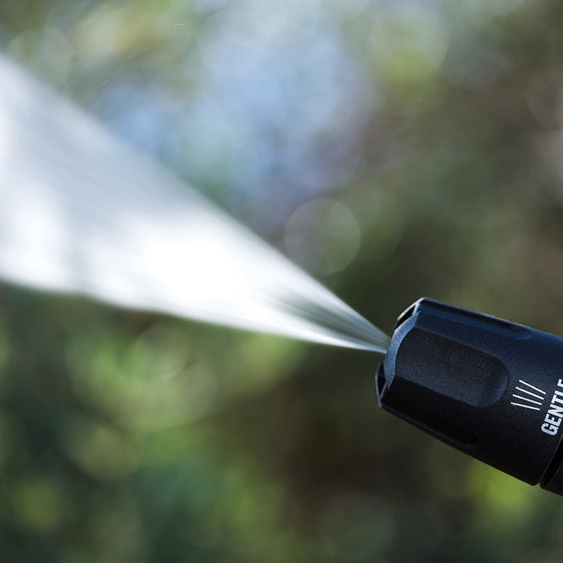 Black pressure washer nozzle from Nilfisk, spraying water against a blurred green background.