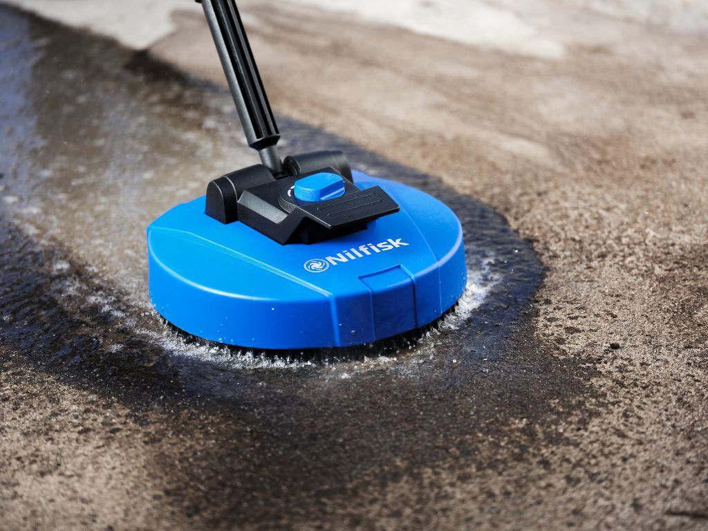 Blue patio cleaner attachment for pressure washers by Nilfisk, removing dirt from a concrete surface.
