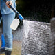 Pressure washer accessory by Nilfisk, cleaning outdoor wicker furniture with foamy water.