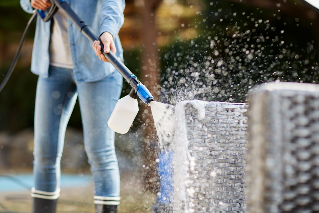 Foam sprayer for pressure washers by ES, attached to a black lance and cleaning a wicker pot.
