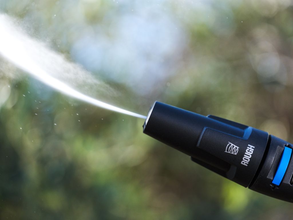Black high-pressure washer by ES, spraying a powerful stream of water against a blurred green background.