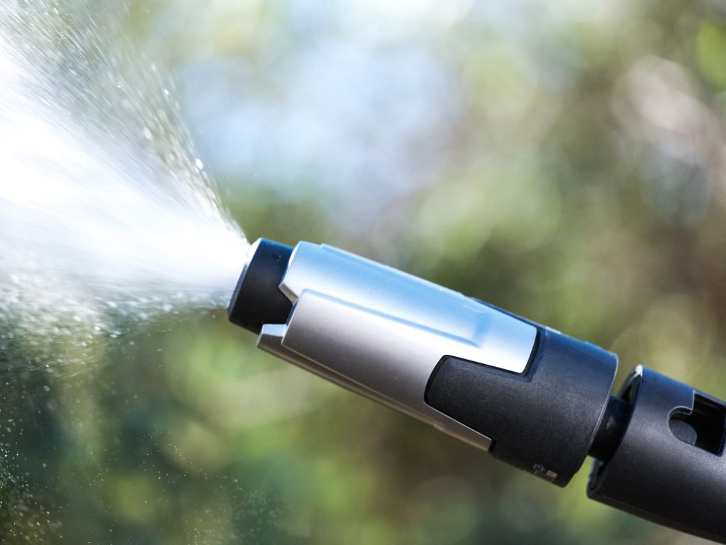 High pressure washer by Nilfisk spraying water out, with a black and silver design.