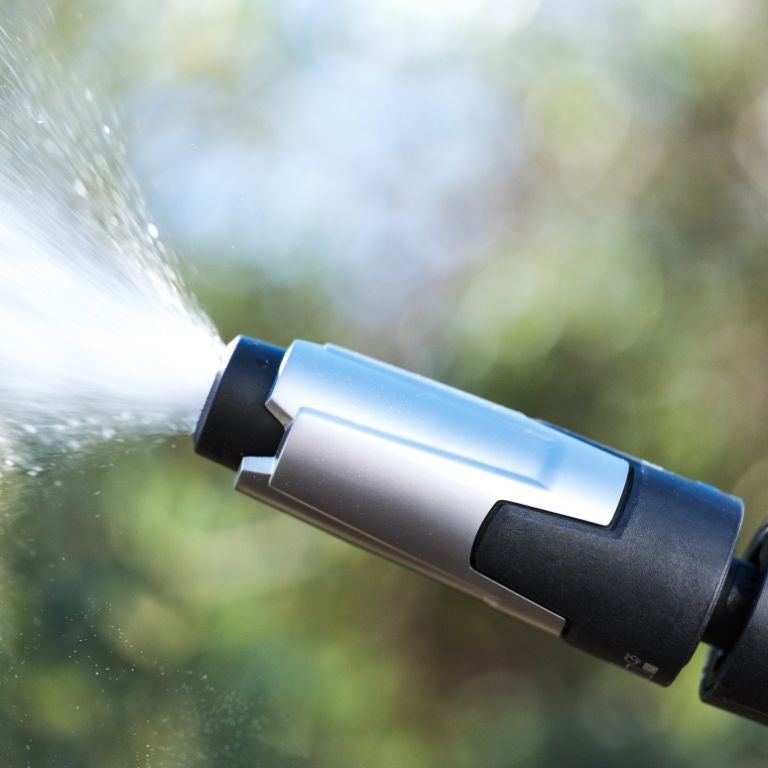 High-pressure cleaner nozzle by UK Premium, expelling water outdoors with a blurred green background.