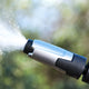 High-pressure cleaner nozzle by UK Premium, expelling water outdoors with a blurred green background.