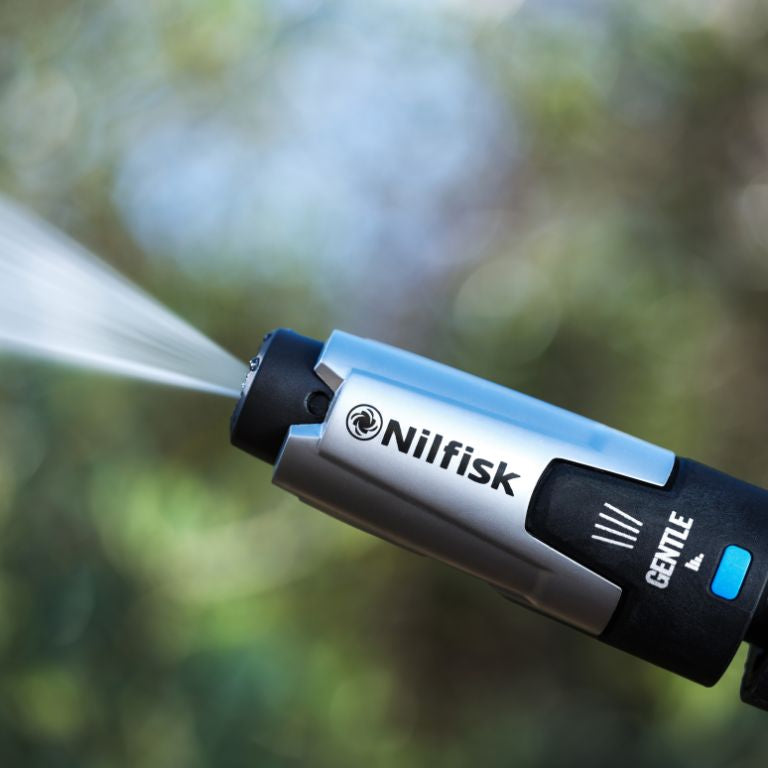 High pressure washer gentle nozzle by Nilfisk with a silver and black finish, and a water jet spraying out.