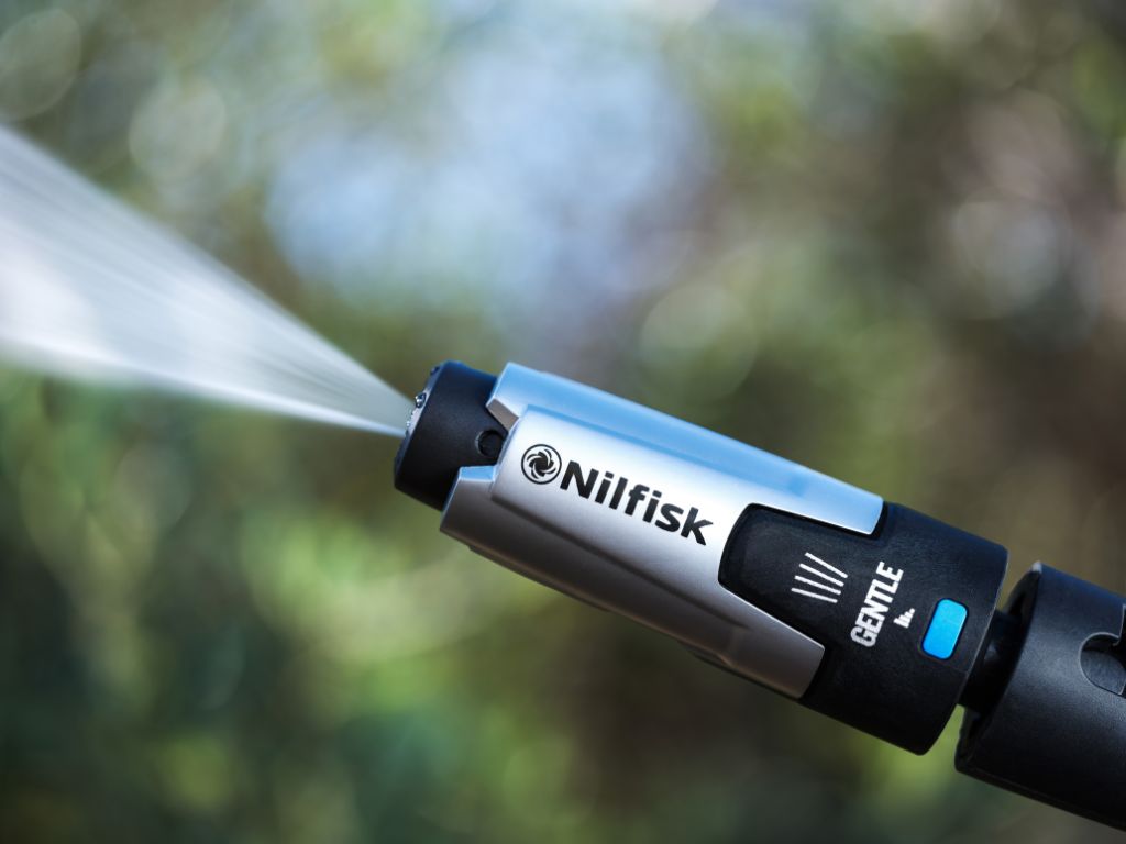 High pressure washer gentle nozzle by Nilfisk with a silver and black finish, and a water jet spraying out.
