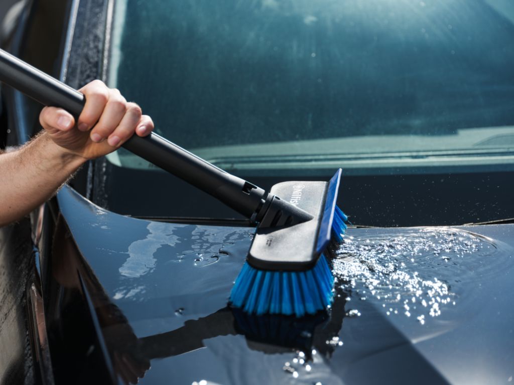 Blue auto brush by UK being used on a shiny black car hood.