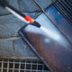 High pressure washer attachment for pressure washers with spray being directed at a dark metal surface.