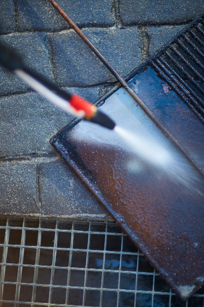 High pressure washer attachment for pressure washers with spray being directed at a dark metal surface.