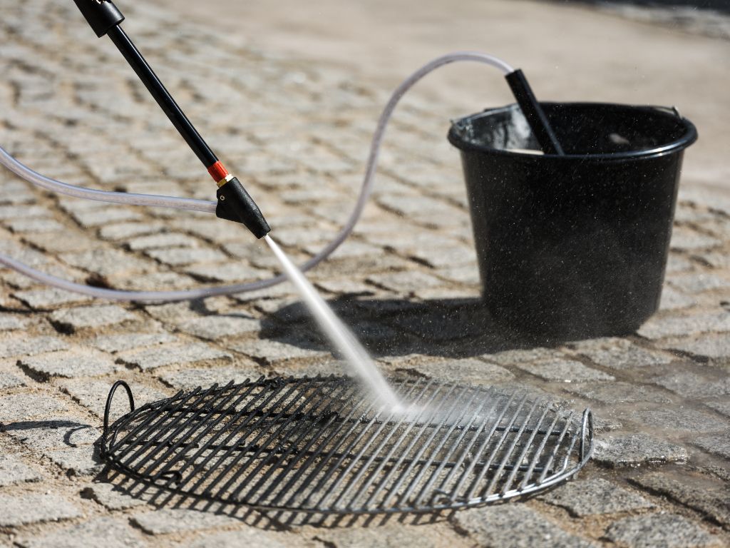 Pressure washer sandblaster accessory for high-pressure cleaners with water stream pointed at metal grid.